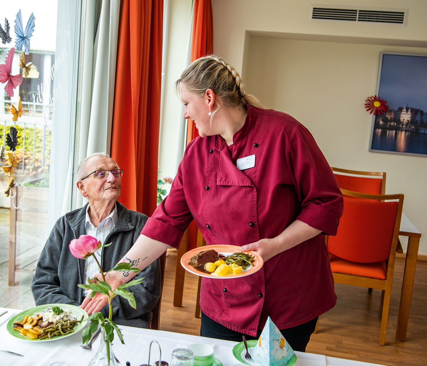 Pflegebedürftiger Bewohner einer Einrichtung der Seniorenpflege bekommt das Essen von einer Mitarbeiterin gebracht.