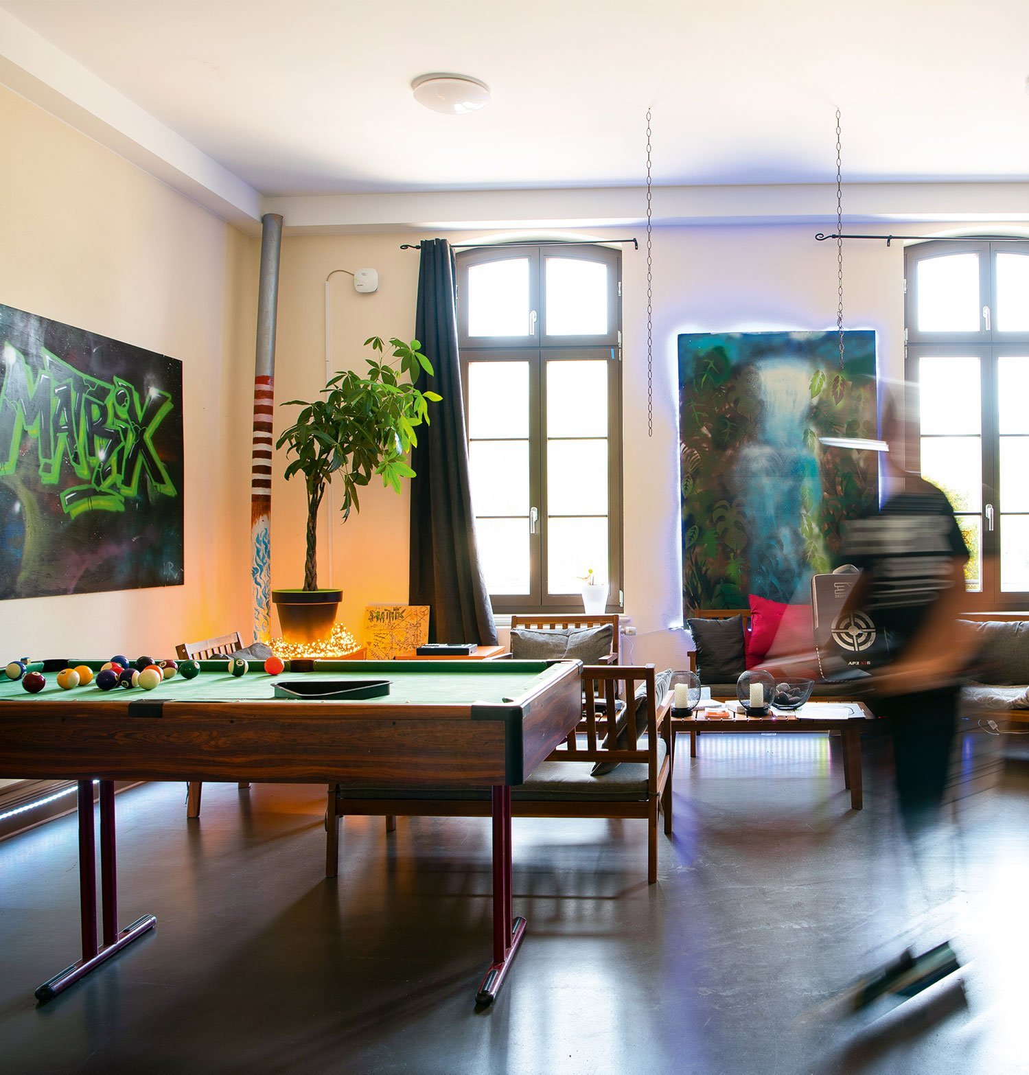 Raum mit Billardtisch, Pflanze, Sitzecke und Poster an Wand.