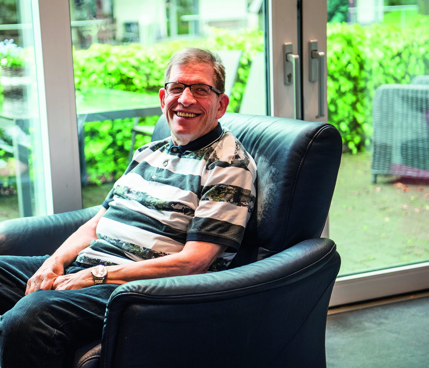 Ein Mann mit Behinderung sitzt in einem Sessel in einer Wohneinrichtung und lächelt