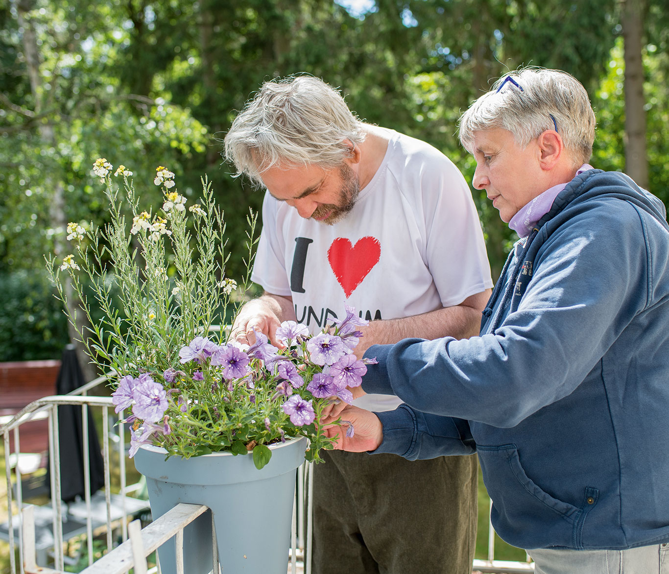 Eine Mitarbeiterin und ein Bewohner der Wohneinrichtung pflegen Blumen auf einem Balkon.