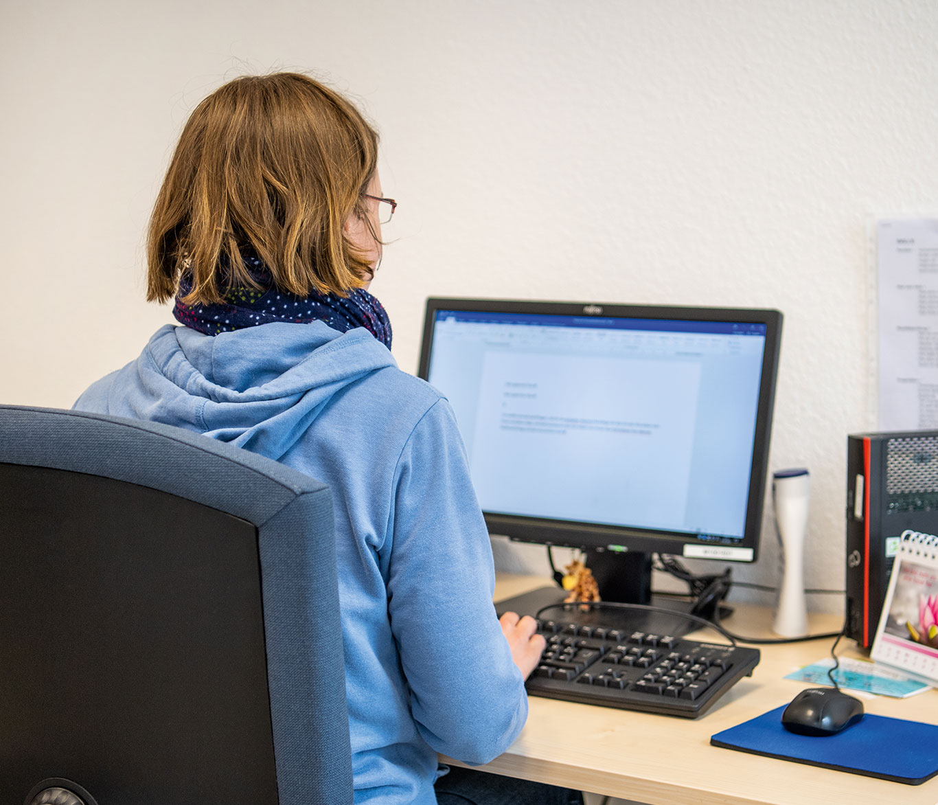 Frau sitzt am Computerarbeitsplatz bei der beruflichen Rehabilitation.