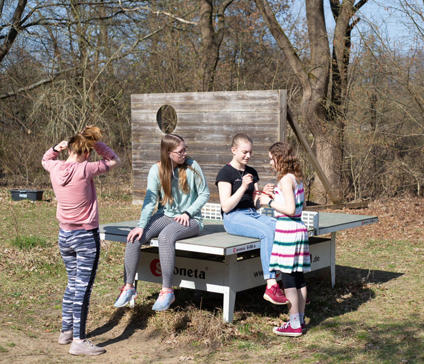 Jugendliche Mädchen einer Wohngruppe der Vorwerker Diakonie sitzen auf und um einen Tischtennisplatte herum und unterhalten sich. 