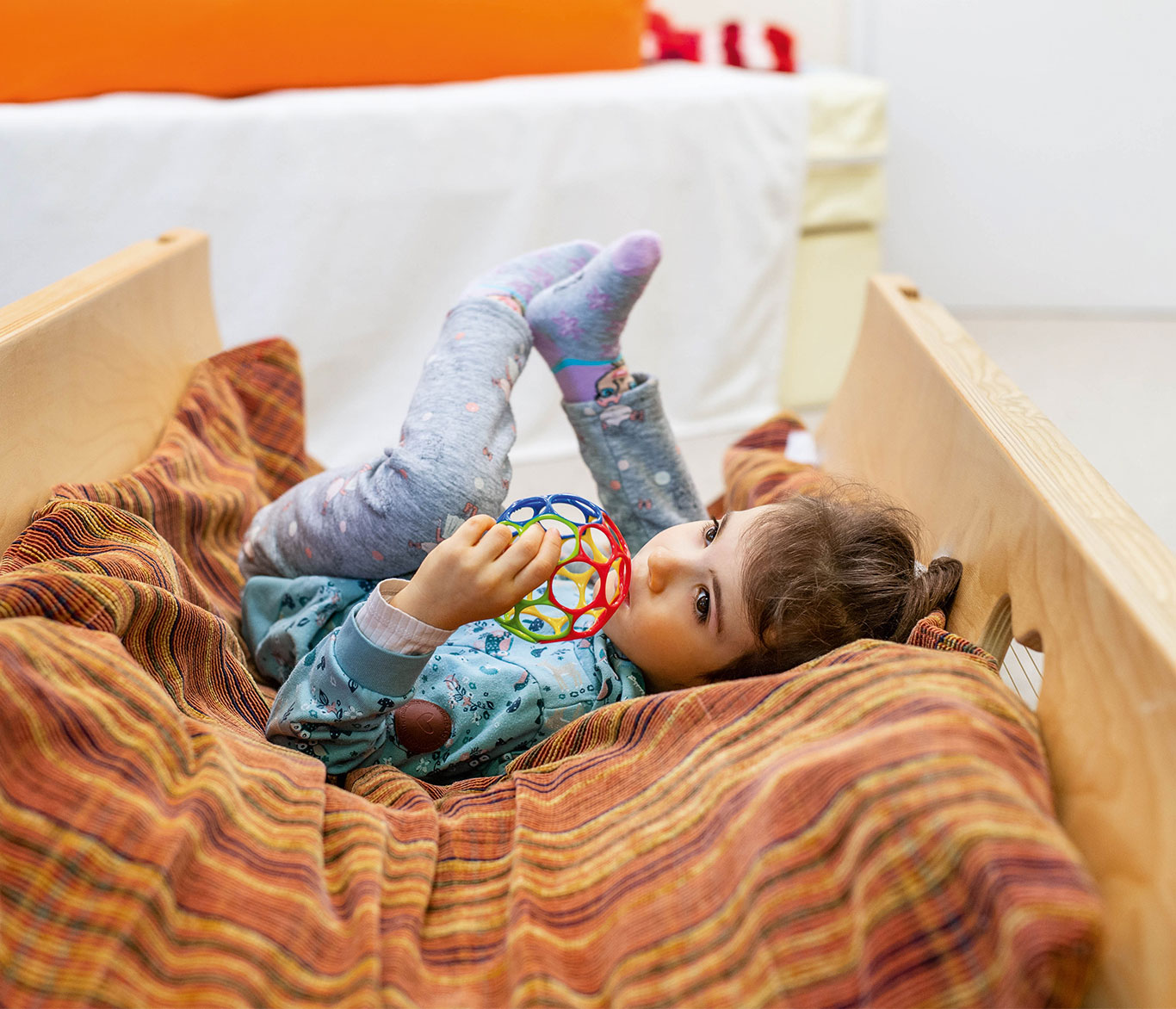 Ein Mädchen liegt in der Kita und Familienzentrum Haus Barbara mit einem Spielzeug auf einem Bett.