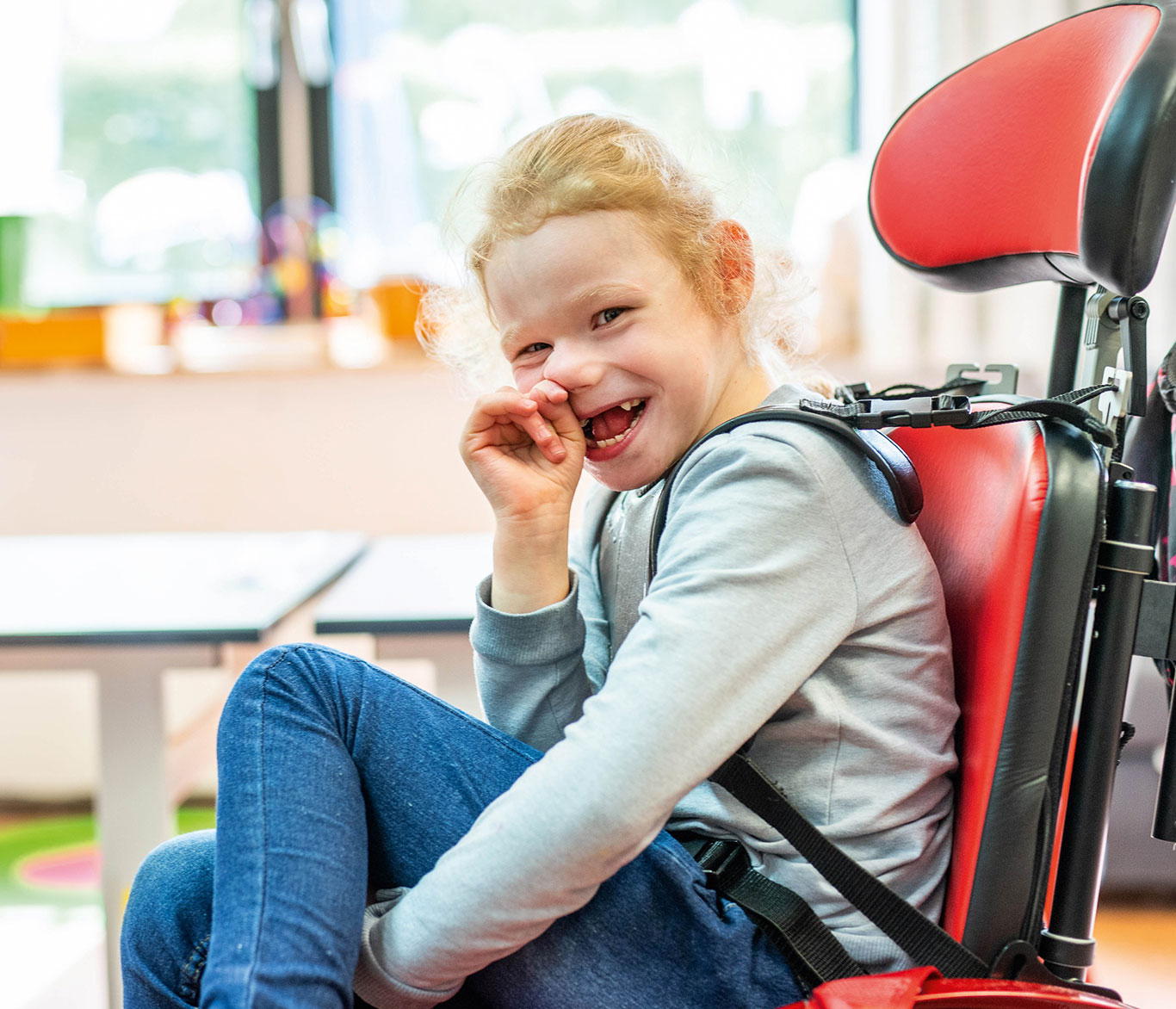 Ein Mädchen mit Behinderung sitzt lächelnd im Rollstuhl. 