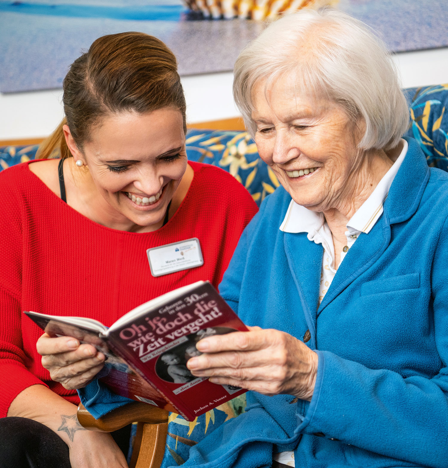 Eine Pflegerin blickt mit einer Seniorin in einer Einrichtung der Seniorenpflege in ein Buch.
