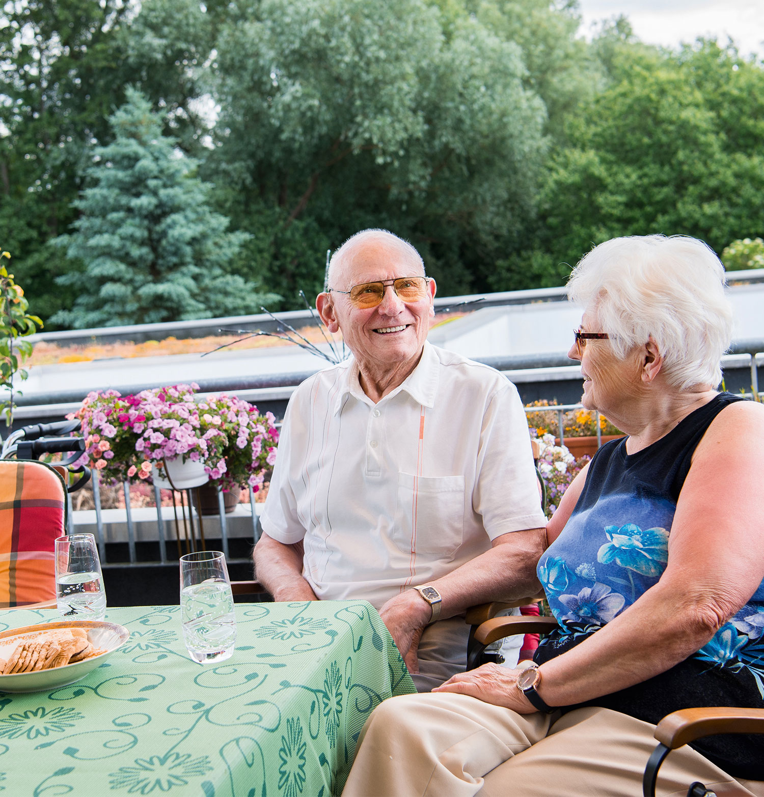 Zwei Senioren sitzen in der Wohnanlage für Wohnen mit Service am Tisch auf ihrem Balkon.