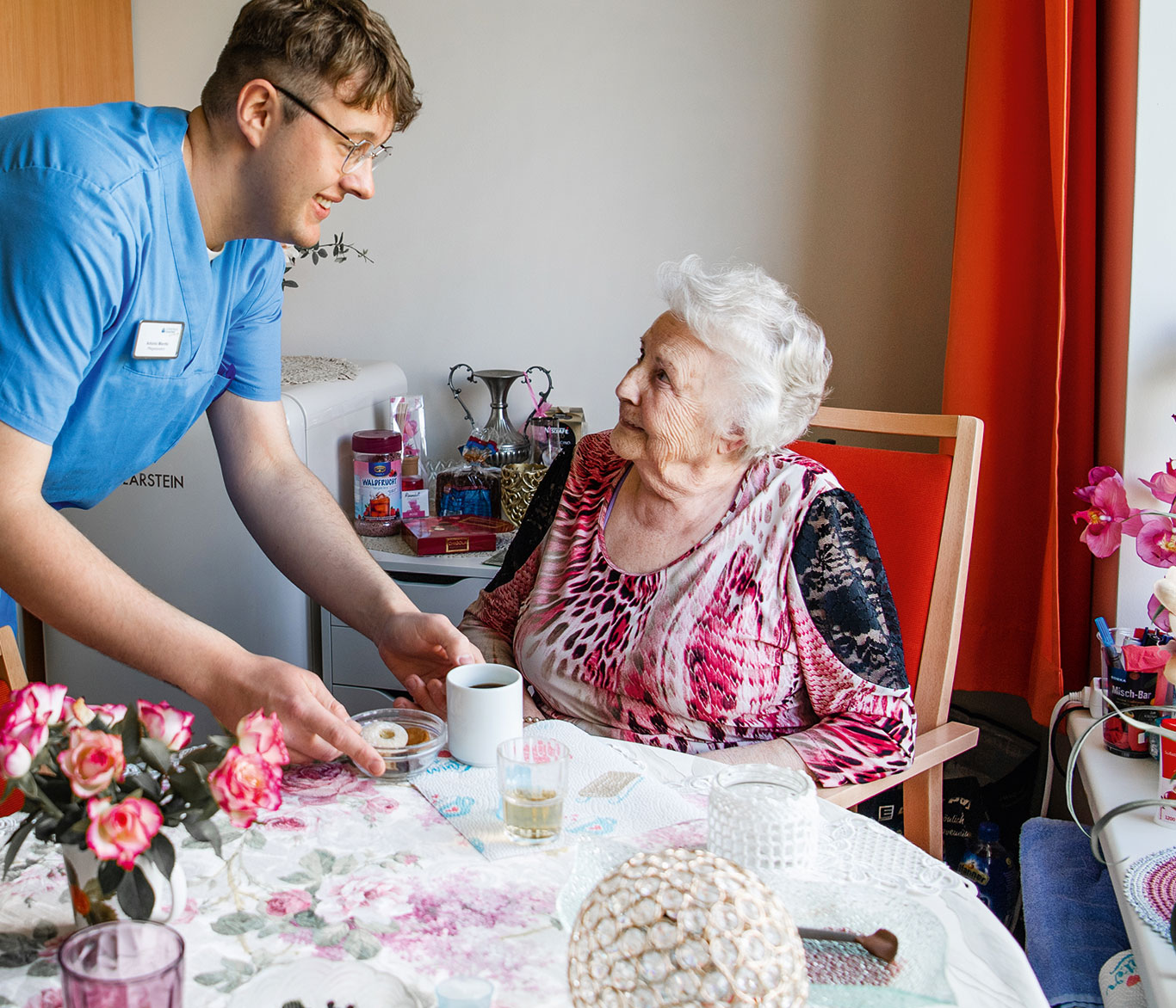 Ein Pfleger bringt einer Pflegebedürftigen in der Einrichtung der Seniorenpflege in Travemünde Kaffee an den Tisch.