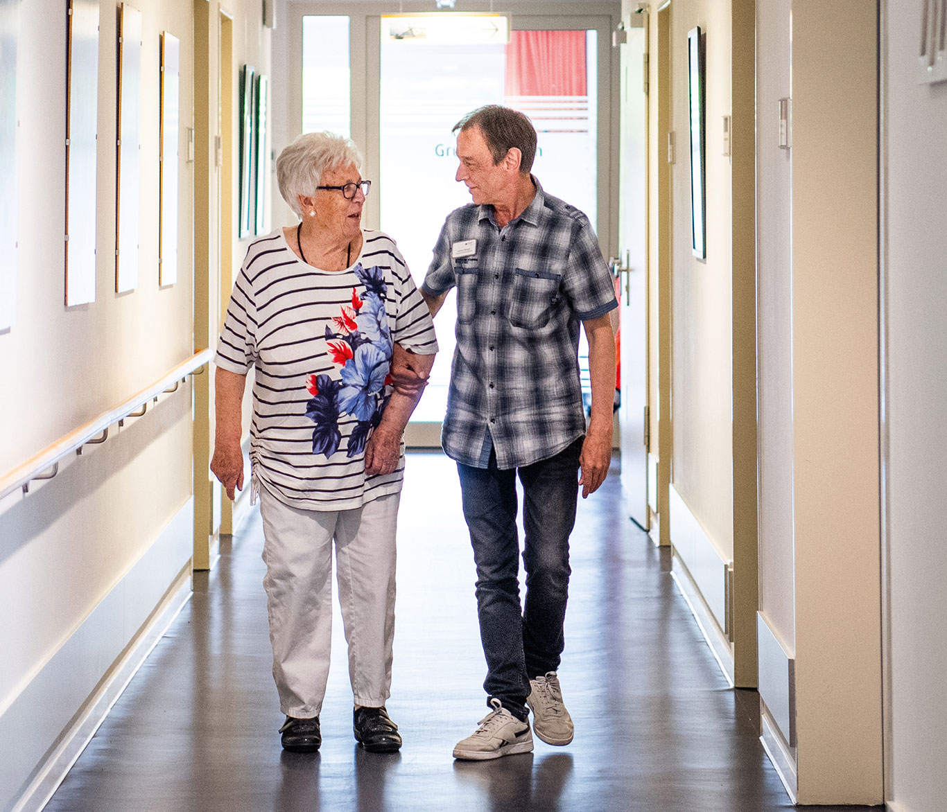 Ein Pfleger geht mit einer Pflegebedürftigen in der Einrichtung der Seniorenpflege in Travemünde den Gang entlang.