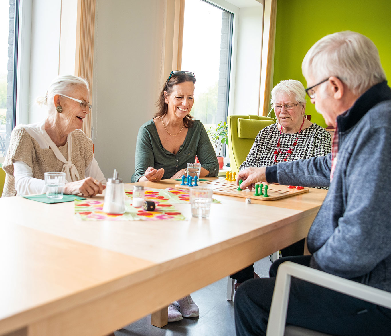 Senioren spielen zusammen mit einer Pflegerin in der Tagespflege der Vorwerker Diakonie ein Brettspiel an einem Tisch.