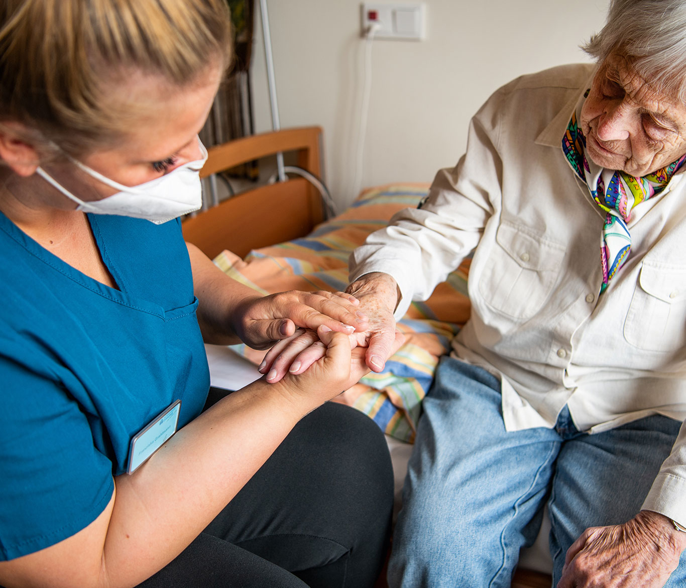 Pflegerin hält die Hand einer Pflegebedürftigen in einer Einrichtung der Seniorenpflege.