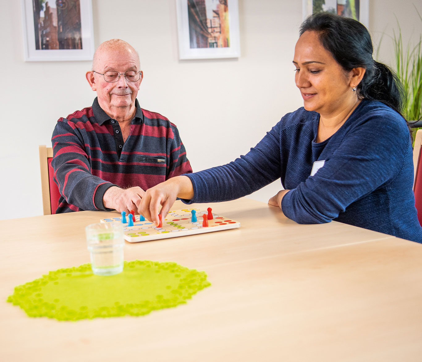 Eine Pflegerin spielt mit einem Pflegebedürftigen ein Brettspiel in einer Einrichtung der Seniorenpflege.