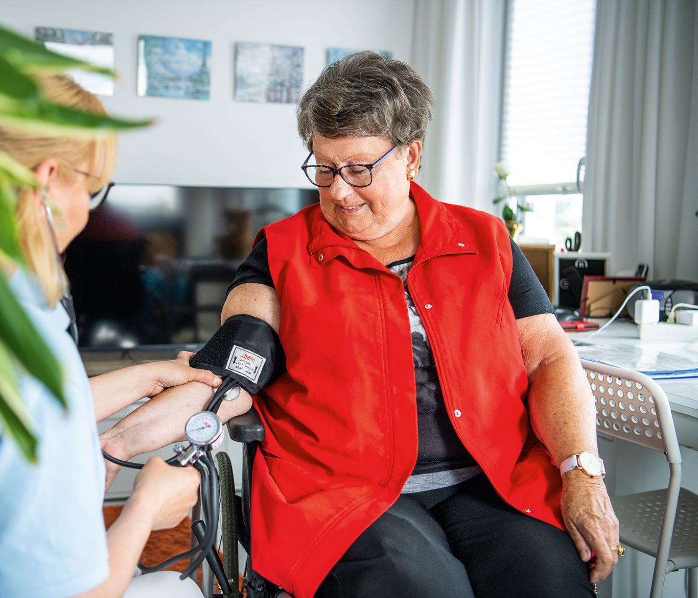 Pflegerin der ambulanten Pflege misst einer Seniorin in ihrem Zuhause den Blutdruck.