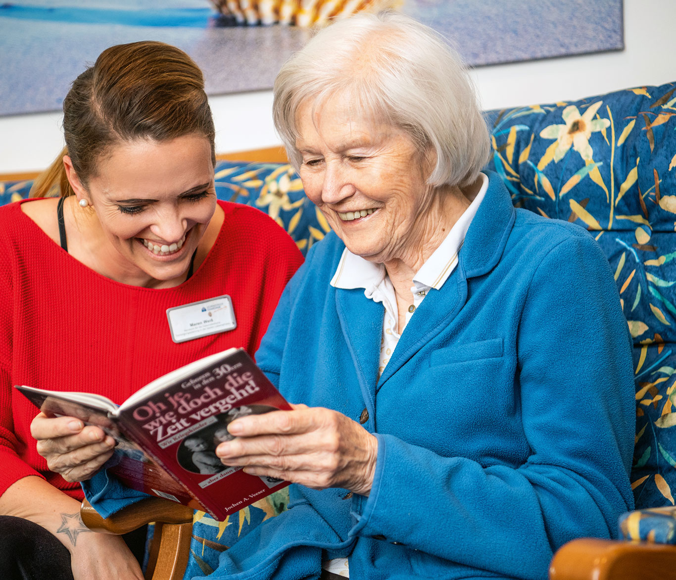 Eine Pflegerin blickt mit einer Seniorin in einer Einrichtung der Seniorenpflege in ein Buch.
