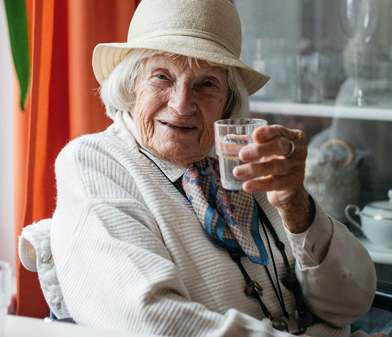Eine Seniorin in einer Einrichtung der Seniorenpflege prostet mit einem Glas zu.