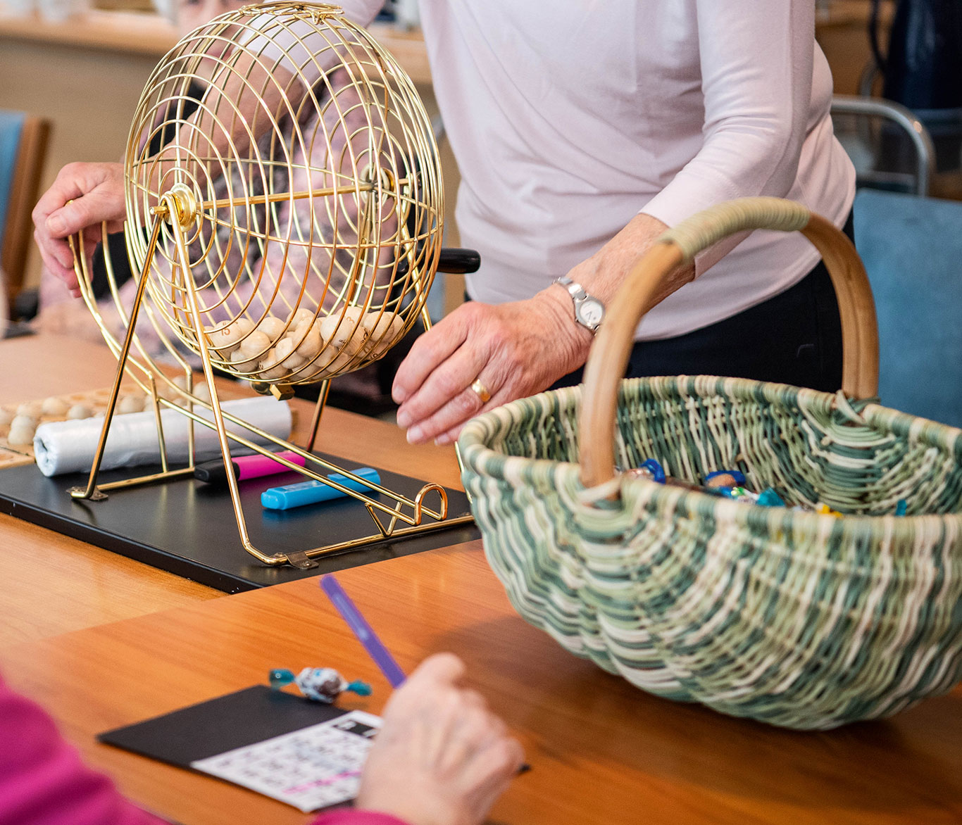 In einer Einrichtung der Seniorenpflege dreht eine Seniorin mit ihren Händen eine Bingo-Mühle.