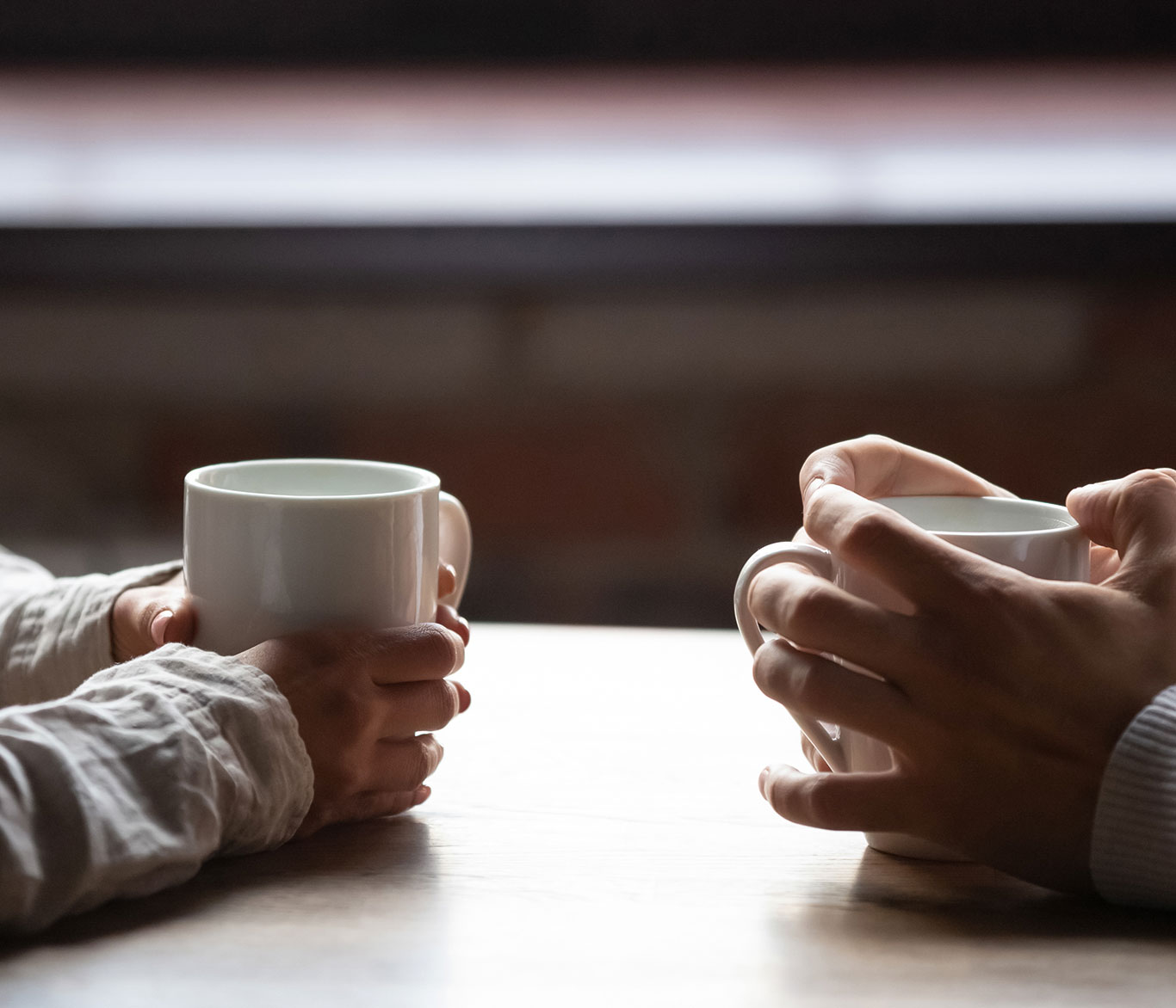 Zwei Menschen sitzen an einem Tisch und halten Kaffeetassen in den Händen.