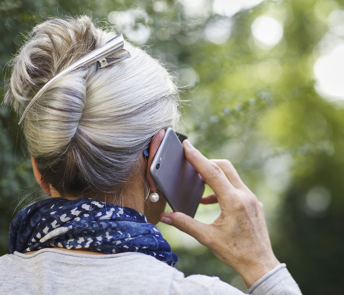 Eine Frau mit grauen Haaren hält ihr Handy ans Ohr und telefoniert.