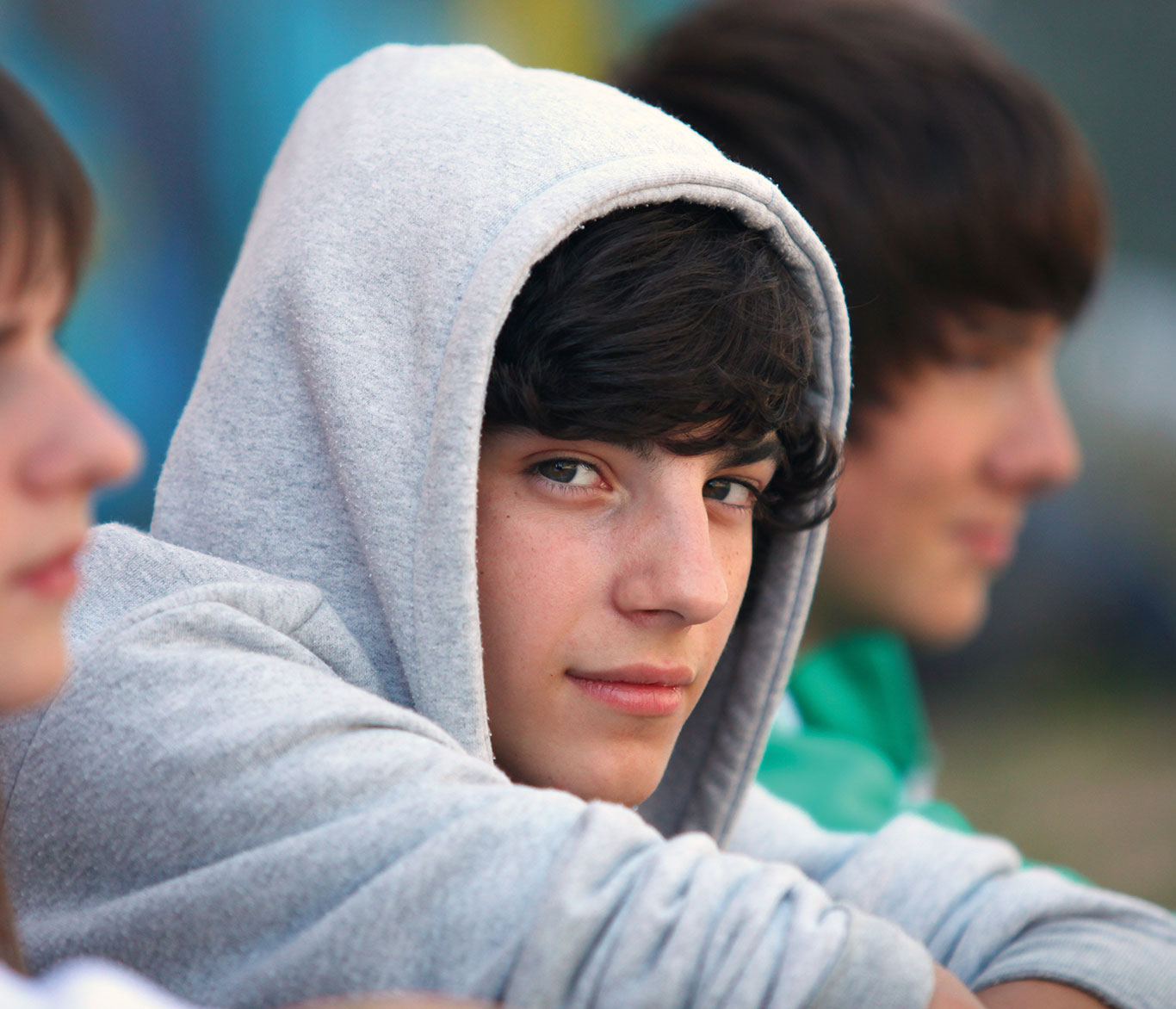 Ein Jugendlicher in grauem Kapuzen-Pullover sitzt zwischen zwei anderen Jugendlichen und schaut in die Kamera.